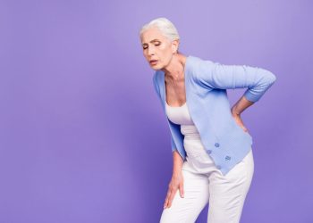 Gray haired old beautiful  woman wearing casual suffering from back pain. Empty blank copy space. Isolated over violet pastel background